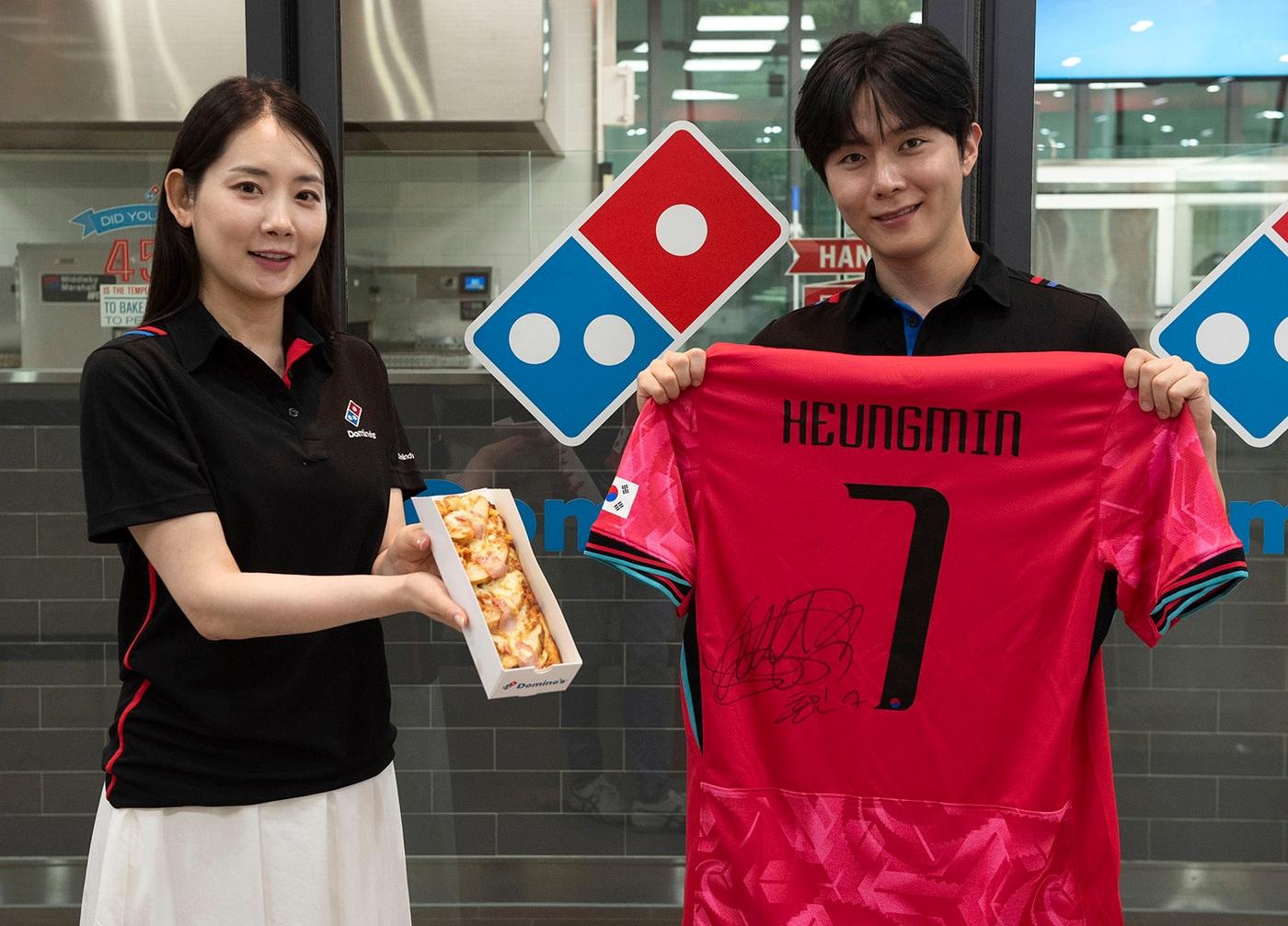 본문 이미지 - 도미노피자 모델이 피자와 손흥민 선수 국가대표 유니폼을 소개하는 모습.&#40;도미노피자 제공&#41;