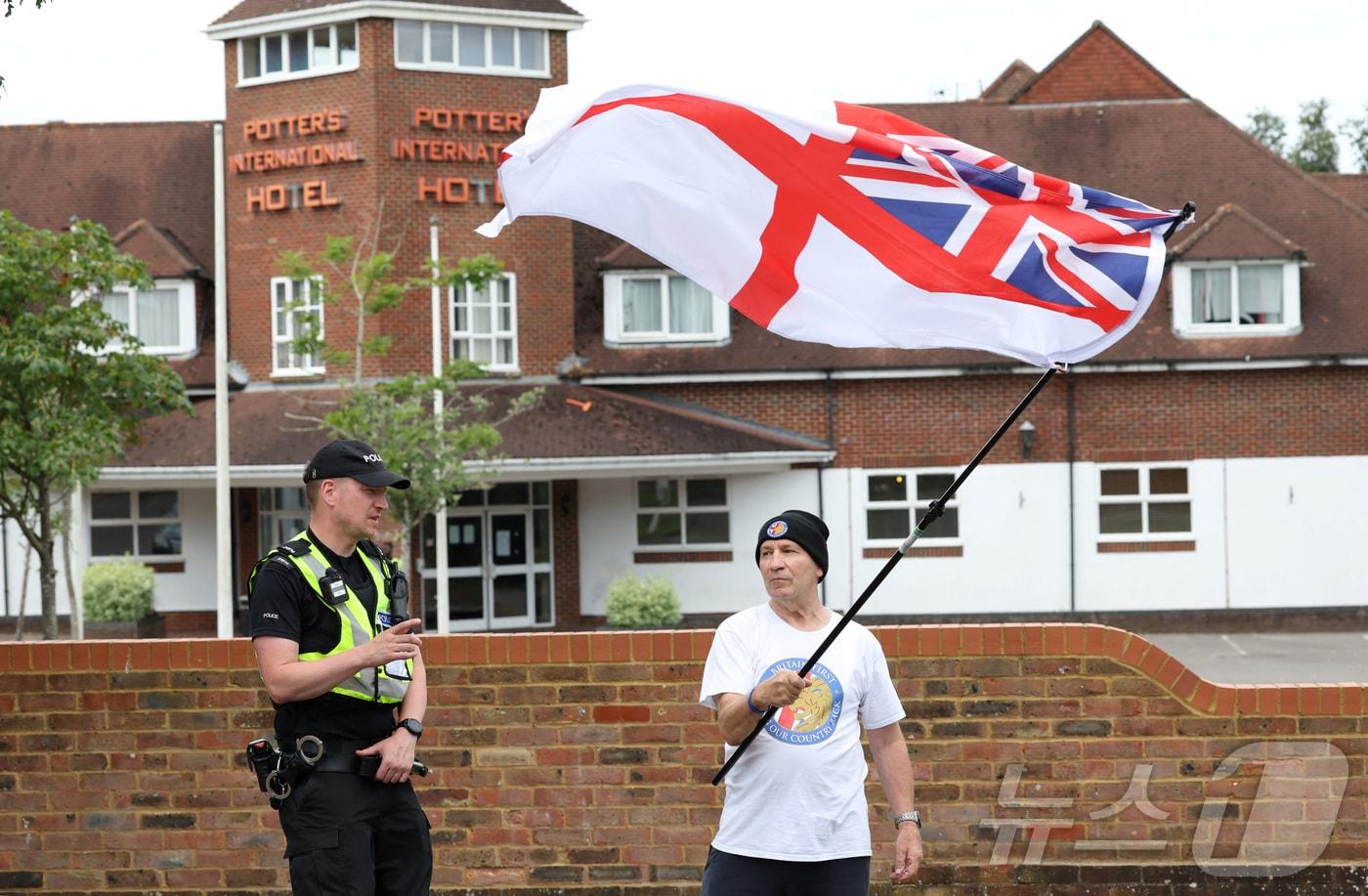 2024년 8월 영국 올더숏에서 열린 반이민 시위에서 한 경찰관이 이민자 수용소 호텔 밖에서 영국 해군기를 흔드는 한 남성에게 자리를 비켜 달라고 요청하고 있다. 2024.8.4 &#40;특정 기사 내용과는 무관한 자료사진&#41; ⓒ 로이터=뉴스1 ⓒ News1 김경민 기자