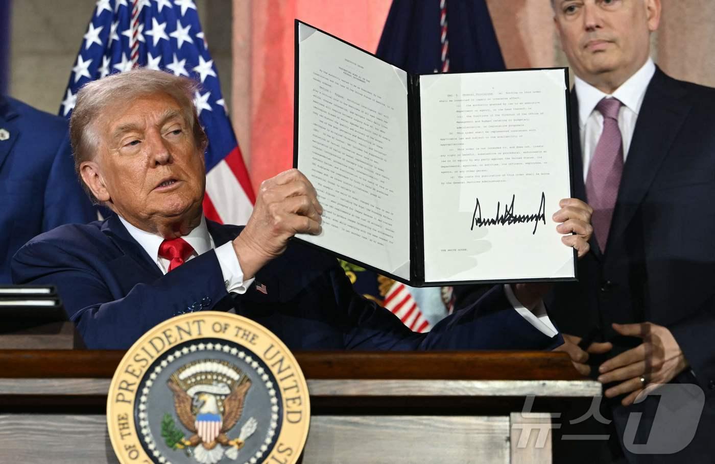 23일&#40;현지시간&#41; 미국 워싱턴 D.C.의 앤드루 W. 멜론 오디토리움에서 열린 ‘AI 경쟁에서 승리하기&#40;Winning the AI Race&#41;’ 정상회의에서 도널드 트럼프 미국 대통령이 AI 관련 행정명령에 서명한 후 이를 공개했다. 이 행정명령은 미국이 글로벌 AI 경쟁에서 우위를 확보하기 위한 전략의 일환으로, 규제 완화와 기술 수출 확대 등을 포함하고 있다. ⓒ AFP=뉴스1 
