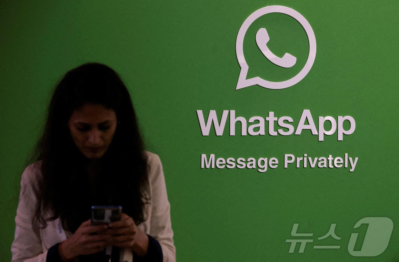한 여성이 왓츠앱(WhatsApp) 로고 옆에서 휴대폰을 사용하고 있다. (특정 기사 내용과는 무관한 자료사진) 2025.02.20. ⓒ 로이터=뉴스1 ⓒ News1 유채연 기자