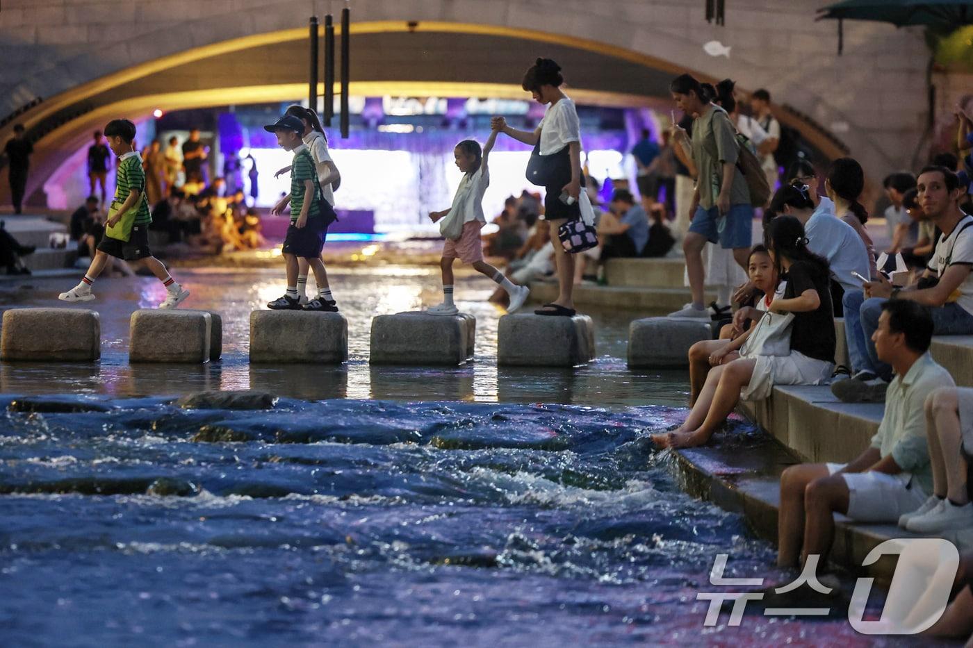 뜨겁고 습한 날씨가 이어지며 열대야 현상 발생이 전망된 30일 저녁 서울 중구 청계천을 찾은 시민들이 물에 발을 담그는 등 산책을 즐기며 무더위를 식히고 있다. 2025.7.30/뉴스1 ⓒ News1 민경석 기자