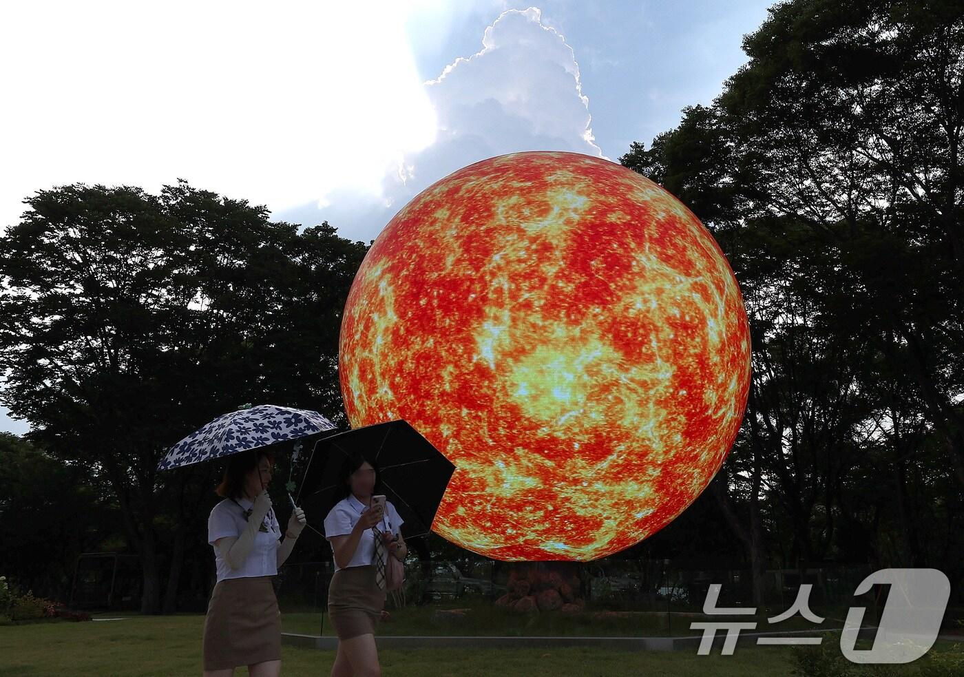 전국 대부분 지역에서 최고 체감온도가 35도 안팎으로 오르며 무더운 날씨가 이어진 8일 서울 송파구의 한 조형물 앞으로 양산을 쓴 시민들이 지나고 있다. 2025.7.8/뉴스1 ⓒ News1 구윤성 기자