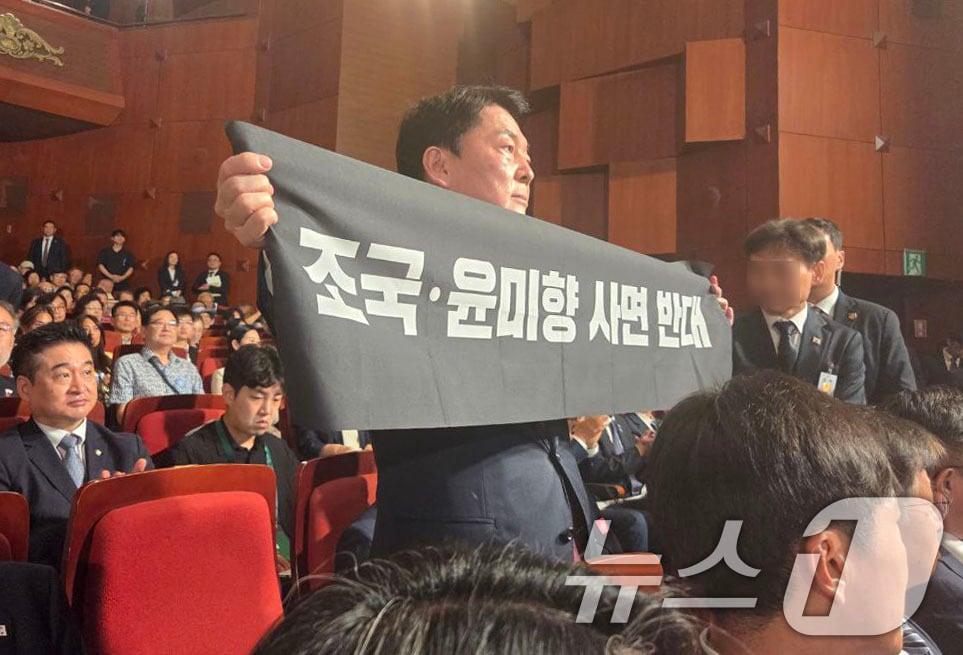 본문 이미지 - 안철수 국민의힘 당대표 후보가 15일 오전 서울 종로구 세종문화회관에서 열린 제80주년 광복절 경축식에 참석해 경축사 중인 이재명 대통령을 향해 조국 전 조국혁신당 대표와 윤미향 전 의원의 사면 반대 플래카드를 들어보이며 항의하고 있다. (안철수 캠프 제공) 2025.8.15/뉴스1