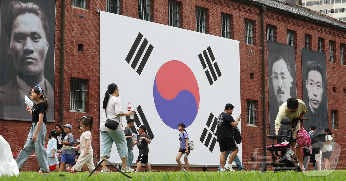 본문 이미지 - 제80주년 광복절인 15일 서울 서대문형무소역사관을 찾은 어린이들과 관람객들이 대형 태극기와 독립운동가들의 얼굴이 담긴 현수막 앞을 지나고 있다. 2025.8.15 ⓒ 뉴스1 김진환 기자