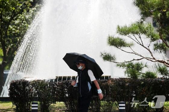 본문 이미지 - 한 시민이 양산을 쓰고 분수대 옆을 지나가고 있다./뉴스1 공정식 기자