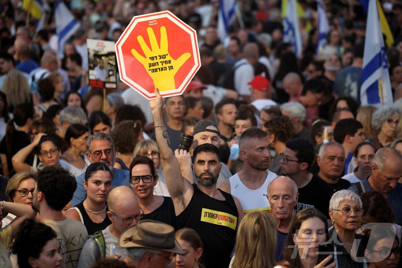 17일(현지시간) 이스라엘 텔아비브 '인질 광장' 일대에서 열린 인질 석방과 가자 전쟁 종식을 촉구하는 집회에서 한 참석자가 "네 아우의 핏소리가 땅에서부터 내게 호소하느니라＂라고 적힌 손팻말을 들고 있다. 2025.08.17. ⓒ 로이터=뉴스1 ⓒ News1 윤다정 기자