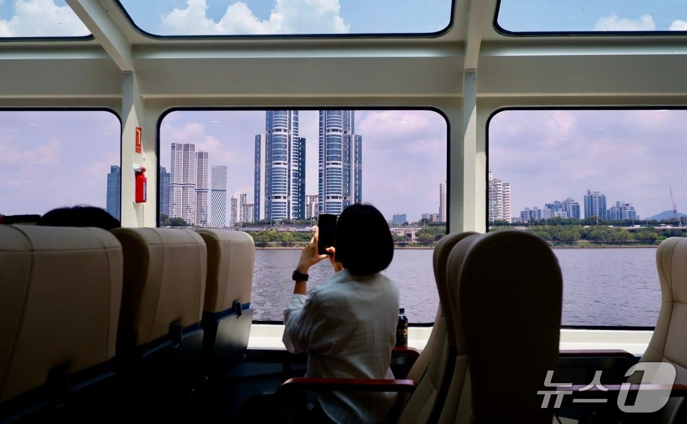 한강버스의 통창을 통해 서울의 풍경을 찍는 탑승객의 모습ⓒ News1 윤슬빈 기자