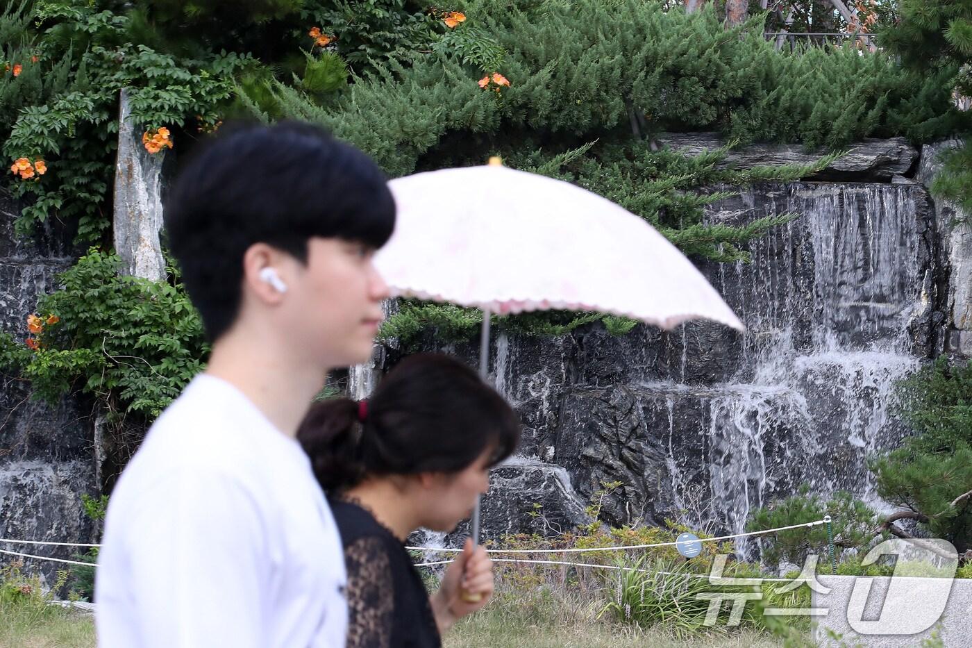 폭염이 계속된 28일 오후 대구 북구의 한 아파트 단지에서 양산을 쓴 시민이 인공폭포 앞을 지나고 있다. 2025.8.28/뉴스1 ⓒ News1 공정식 기자