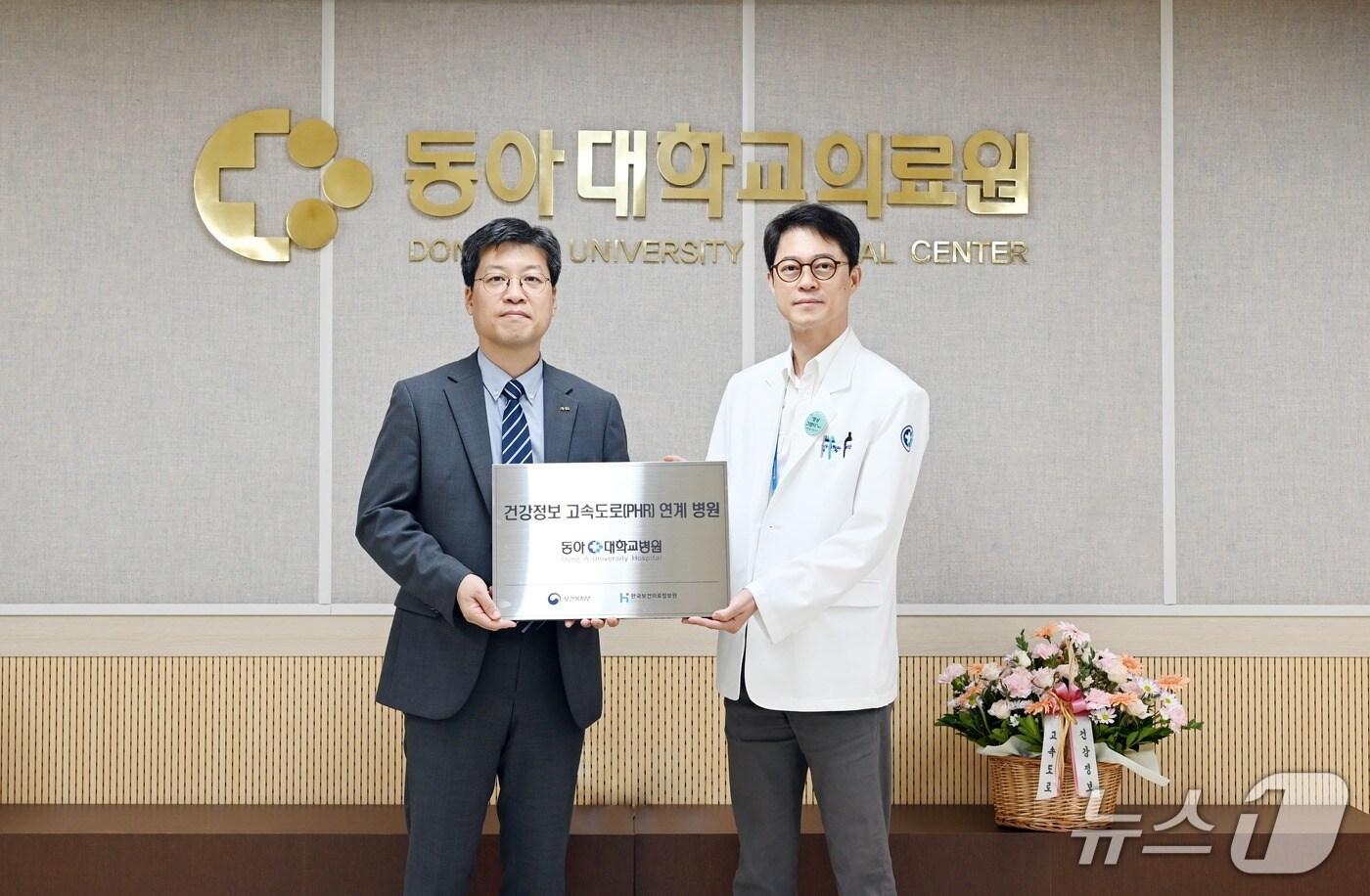 장민철 한국보건의료정보원 PHR사업단장&#40;왼쪽&#41;과 강명진 동아대병원 의료정보센터소장이 건강정보 고속도로 사업 현판을 전달한 뒤 기념촬영을 하고 있다.&#40;동아대병원 제공. 재판매 및 DB 금지&#41;