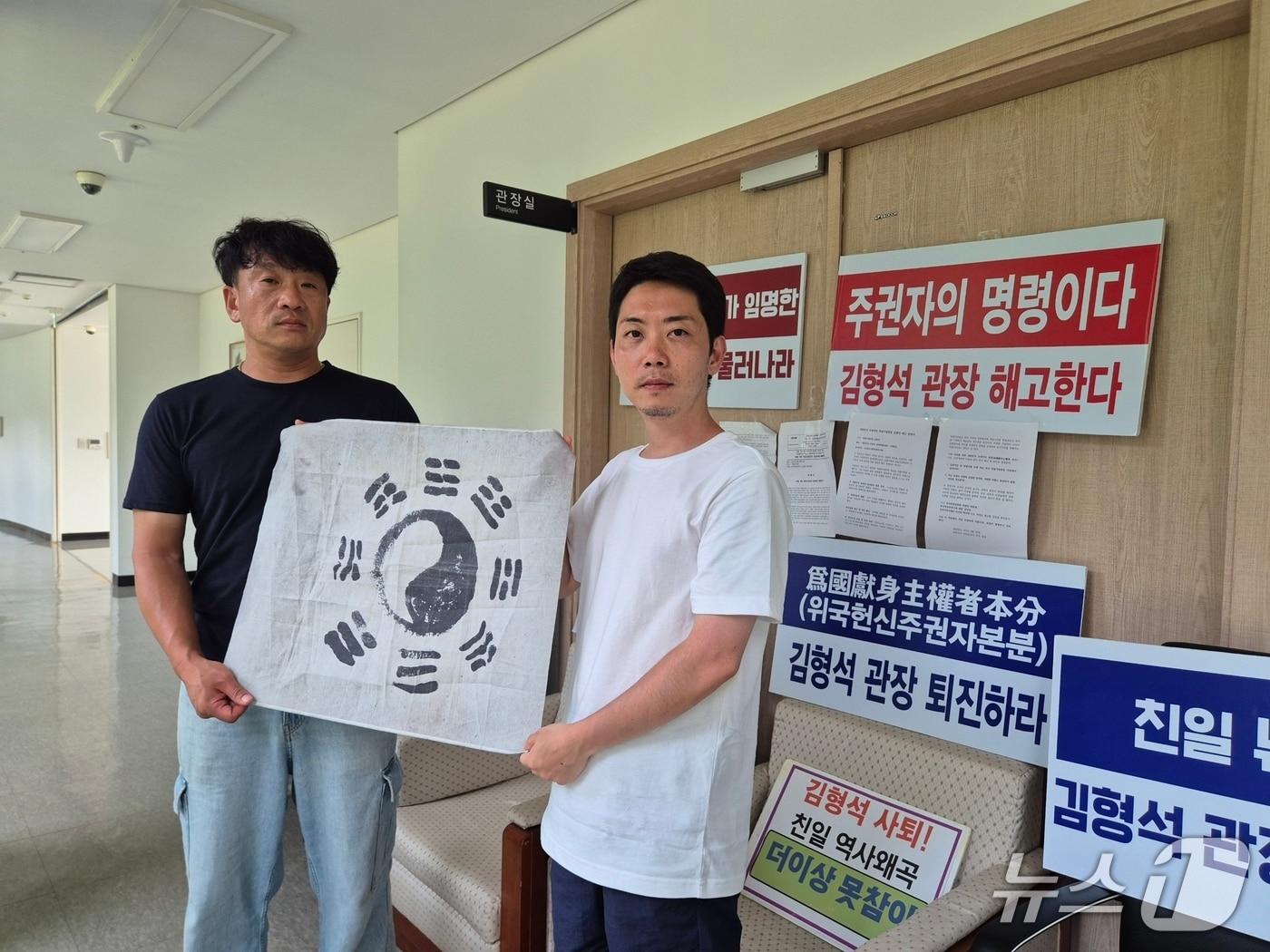 본문 이미지 - 독립기념관장실 점거 농성 중인 김원일 씨(왼쪽)와 오주현 씨가 관장실 앞에서 태극기를 들고 역사왜곡 청산 의지를 다졌다. /뉴스1