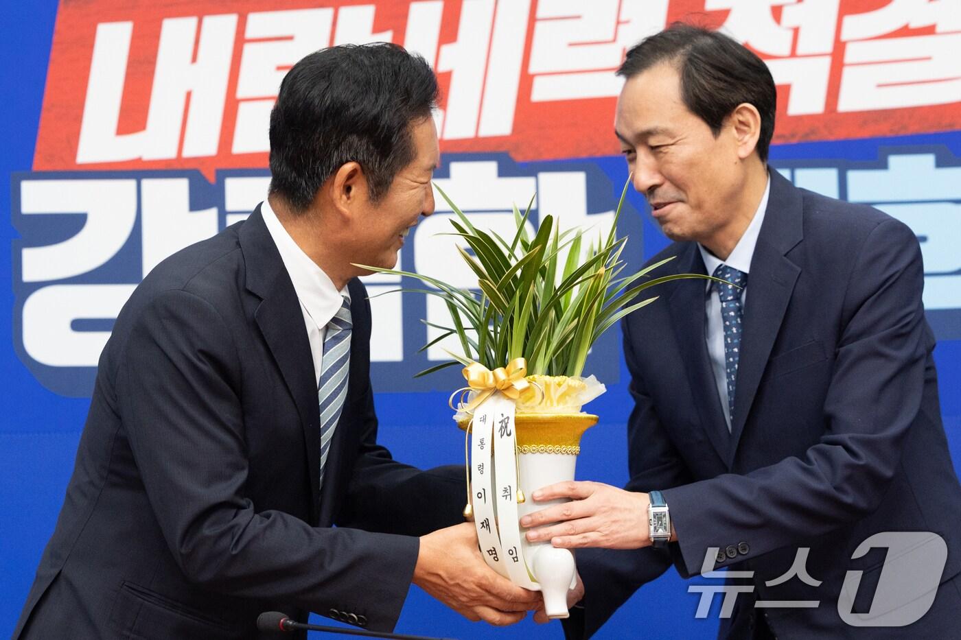 정청래 더불어민주당 신임 대표가 4일 오후 서울 여의도 국회에서 우상호 대통령실 정무수석으로부터 대통령 축하 난을 받고 있다. 2025.8.4/뉴스1 ⓒ News1 이승배 기자