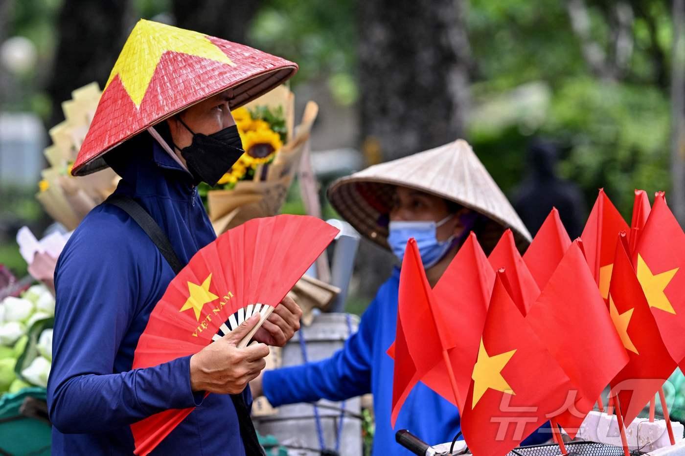 5일 베트남 하노이에서 한 거리 상인이 작은 베트남 국기를 진열해 놓은 옆에서 부채질을 하며 더위를 식히고 있다.  2025.08.05. ⓒ AFP=뉴스1 ⓒ News1 권영미 기자