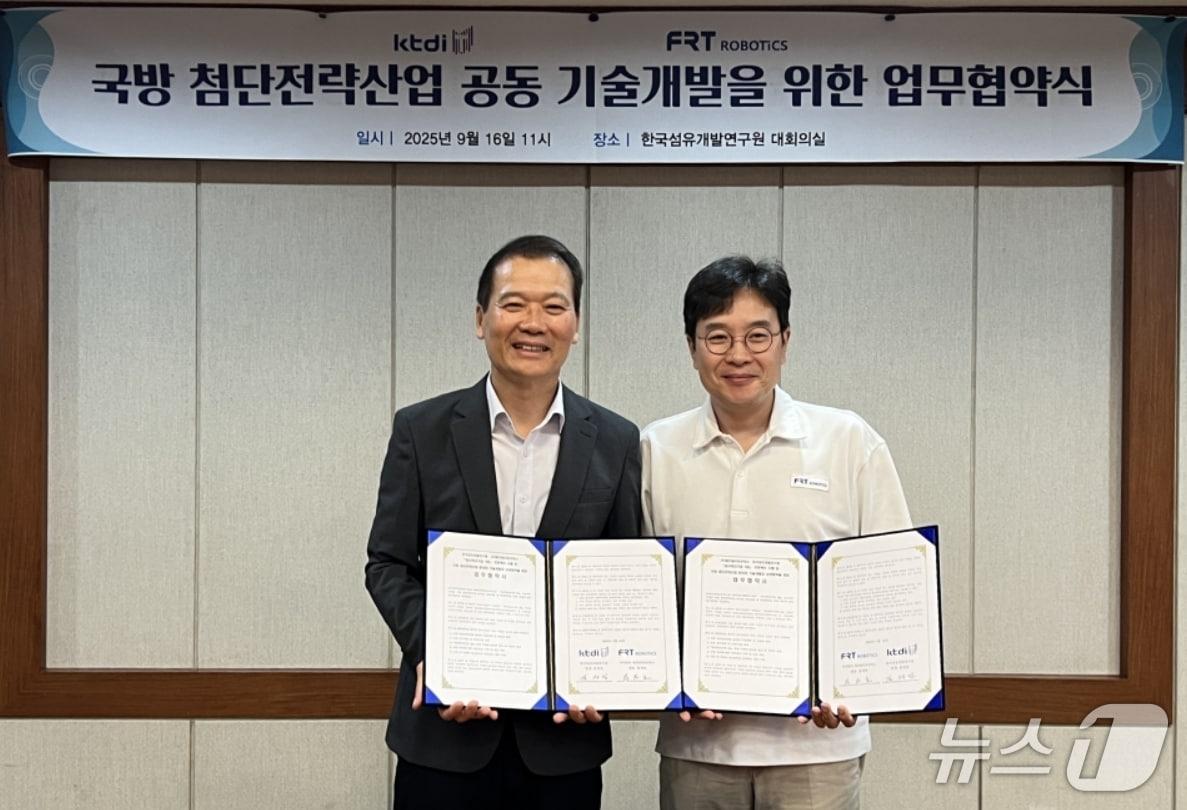 본문 이미지 - 김성만 한국섬유개발연구원장(왼쪽)과 장재호 ㈜에프알티로보틱스 대표가 국방 첨단전략산업 분야 공동 기술개발을 위한 업무협약을 체결한 뒤 협약서를 펼쳐 보이고 있다.(섬유개발연구원 제공. 재판매 및 DB 금지)