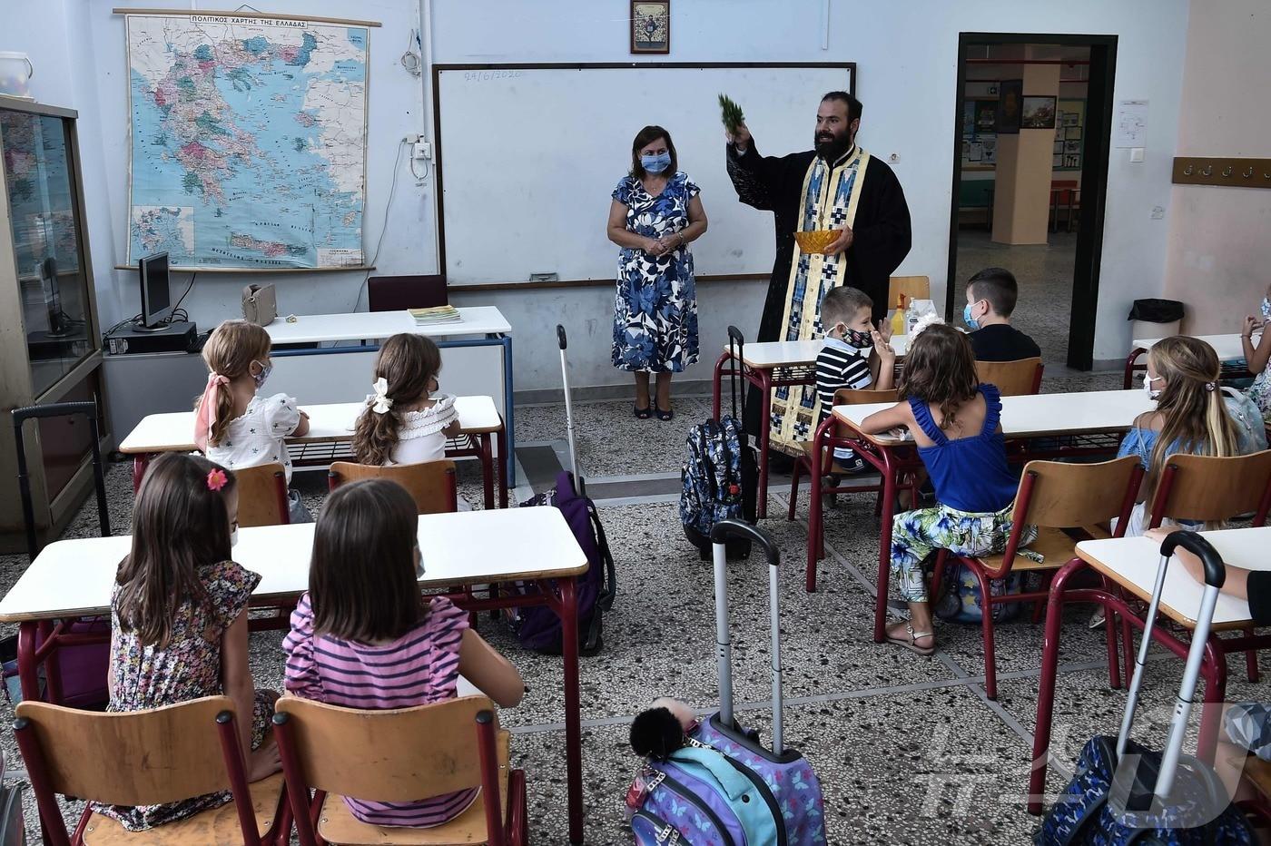 그리스 테사로니키의 초등학교에서 한 성직자가 개학 후 첫 수업 시작 학생들에게 성수를 뿌리며 축복하고 있다. 2020.9.14. ⓒ AFP=뉴스1