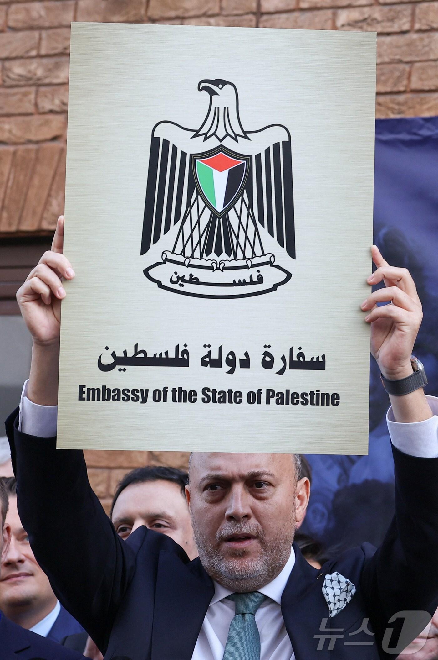 본문 이미지 - 후삼 좀로트 주영 팔레스타인 대표가 22일(현지시간) 영국의 팔레스타인 국가 승인을 기념해 국기게양식을 진행하고 '팔레스타인 대사관' 명판을 들고 있다. 2025.9.22. ⓒ 로이터=뉴스1