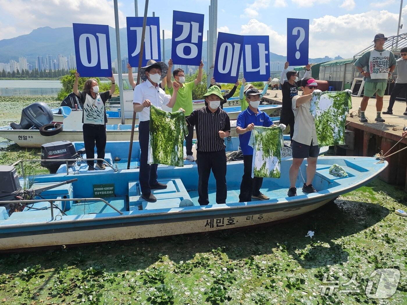 본문 이미지 - 환경단체가 3일 김해시 대동면 대동선착장에서 흰 티셔츠를 강물에 적신 뒤 녹조 심각성을 알리고 있다. 2025.9.3 ⓒ 뉴스1 박민석 기자