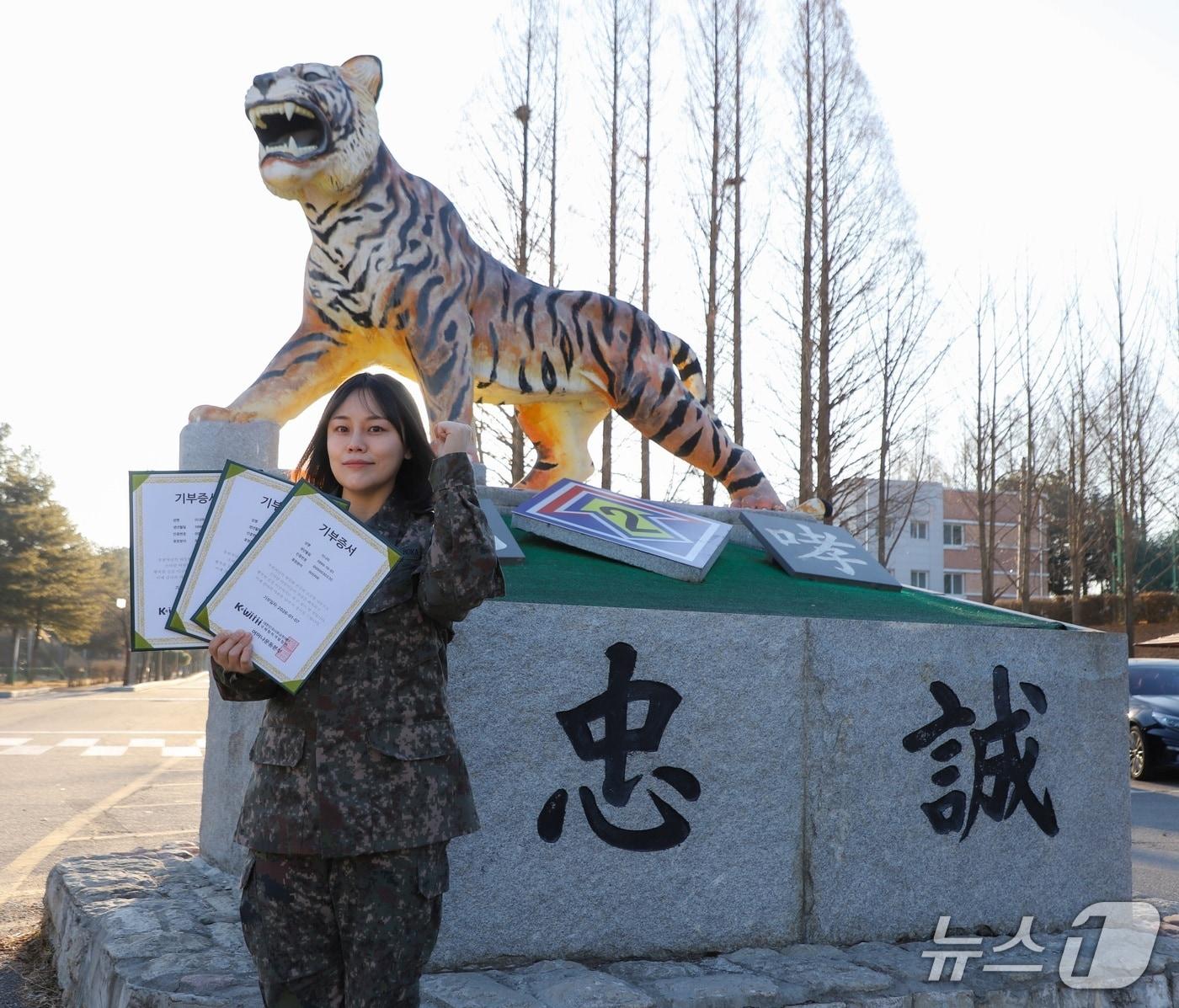 본문 이미지 - 육군 2기갑여단 적오대대 이나라 중사가 부대를 상징하는 호랑이상 앞에서 기부증서를 들고 화이팅 포즈를 취하고 있다. (2기갑여단 제공, 재판매 및 DB금지)