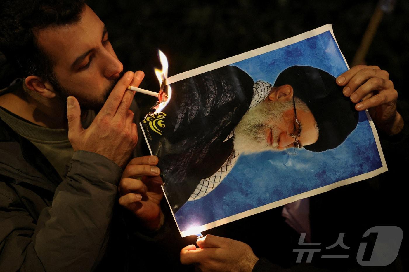 12일(현지시간) 영국 런던 이란 대사관 앞에서 열린 이란 반(反)정부 시위 연대 집회에서 한 참가자가 이란 최고지도자 아야톨라 알리 하메네이의 사진을 불태워 담뱃불을 붙이고 있다. 2025.01.12. ⓒ 로이터=뉴스1 ⓒ News1 윤다정 기자