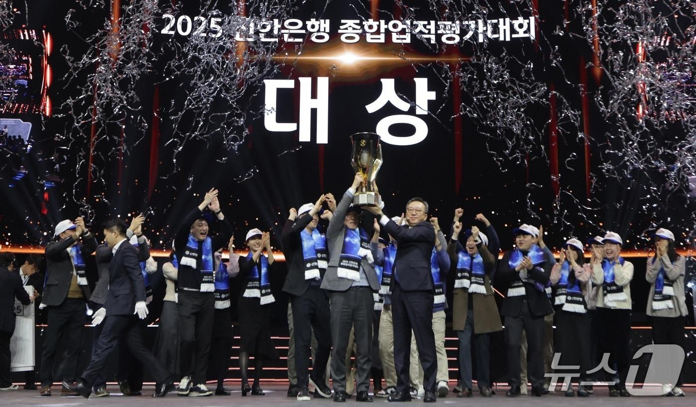 본문 이미지 - 지난 17일 인천광역시 중구 소재 인스파이어 엔터테인먼트 리조트 아레나에서 개최한 ‘2025년 종합업적평가대회’에서 정상혁 신한은행장(가운데 오른쪽)과 박현종 센터장(가운데 왼쪽)이 챔피언 트로피를 들어올리는 모습/사진제공=신한은행