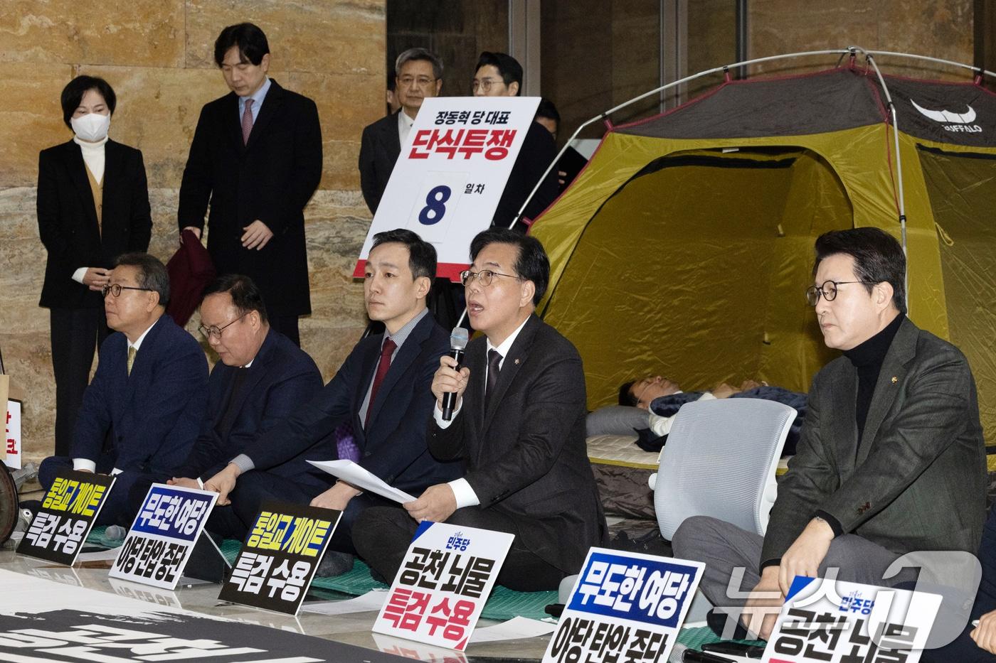본문 이미지 - 송언석 국민의힘 원내대표가 22일 서울 여의도 국회 로텐더홀에서 열린 최고위원회의에서 모두발언하는 가운데 단식 중인 장동혁 대표가 누워서 휴식을 취하고 있다. 2026.1.22/뉴스1 ⓒ News1 이승배 기자