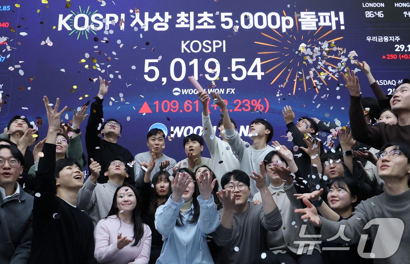 본문 이미지 - 한국 증시가 사상 처음으로 '코스피 5000' 쾌거를 달성한 22일 서울 중구 우리은행 본점 딜링룸에서 직원들이 장중 최고가가 찍힌 전광판을 배경으로 코스피 5000 돌파를 축하하고 있다. 이날 코스피는 이재명 대통령이 '코스피 5000' 공약을 내걸고 임기를 시작한 지 7개월 만에 장중 꿈의 5000을 돌파하며 한국 자본시장의 역사를 새로 썼다. 2026.1.22/뉴스1 ⓒ News1 오대일 기자