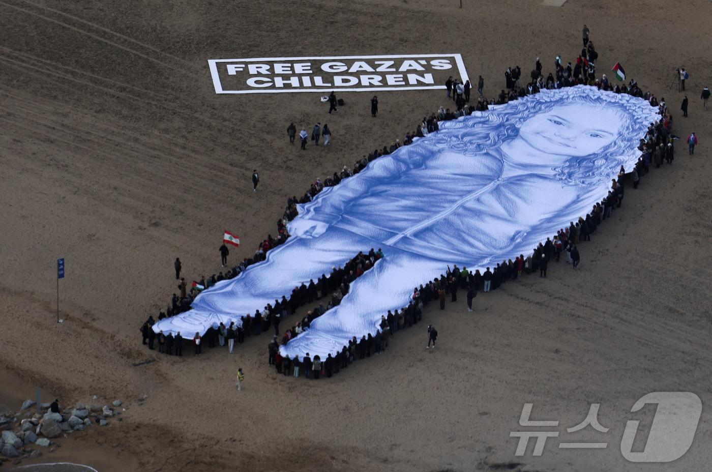 본문 이미지 - 2024년 가자지구에서 사망한 5세 팔레스타인 소녀 힌드 라잡의 거대한 초상화가 29일(현지시간) 바르셀로나 바르셀로네타 해변에 펼쳐졌다. 2026.1.29 ⓒ 로이터=뉴스1 ⓒ News1 김경민 기자