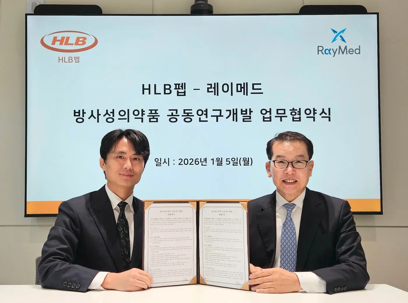 본문 이미지 -  심경재 HLB펩 대표이사(사진 왼쪽)와 김영현 레이메드 대표이사가 '방사성의약품 공동연구개발 업무협약'을 체결하고 기념 촬영을 하고 있다. (HLB펩 제공)