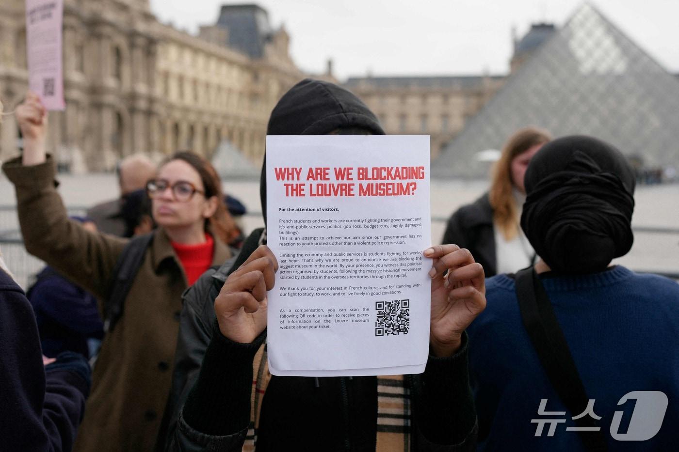 본문 이미지 - 19일(현지시간) '에콜 뒤 루브르'(&Eacute;cole du Louvre) 학생을 비롯한 시위대가 고등학생 시위대에 대한 지지를 표명하며 프랑스 파리 루브르 박물관 입구를 막아선 가운데, 한 청년이 방문객들에게 폐관을 알리는 플래카드를 들어 보이고 있다. 2026.10.19. ⓒ AFP=뉴스1 ⓒ AFP=뉴스1