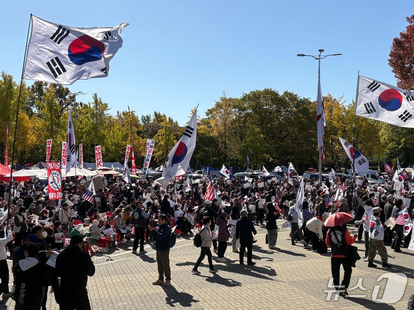 본문 이미지 - 28일 서울 송파구 올림픽공원 핸드볼경기장 1-3게이트 앞에서 6·3 지방선거 투표지 임의검증과 관련해 집회 참가자들이 태극기와 성조기 등을 흔들며 집회를 이어가고 있다. 2026.10.28/뉴스1 소봄이 기자