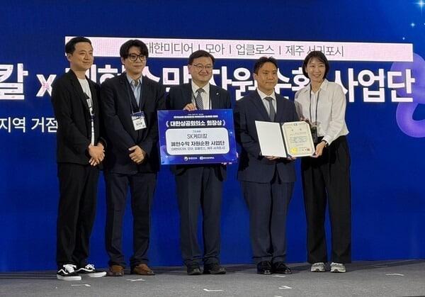 본문 이미지 - 2026년 9월 21일 서울 강남구 코엑스에서 개최된 '제2회 지역-기업 협업 지역사회 문제해결 아이디어 솔버톤 대회'에서 SK케미칼 폐현수막 자원순환 사업단이 대한상공회의소 회장상을 수상했다. (왼쪽부터) 김효진 제주도 서귀포시 생활환경과 자원순환팀장 , 김지훈 대한미디어 김지훈 부사장, 조영준 대한상공회의소 지속가능경영원장, 송병호 모아 대표, 임선아 업클로스 대표 (SK케미칼 제공)