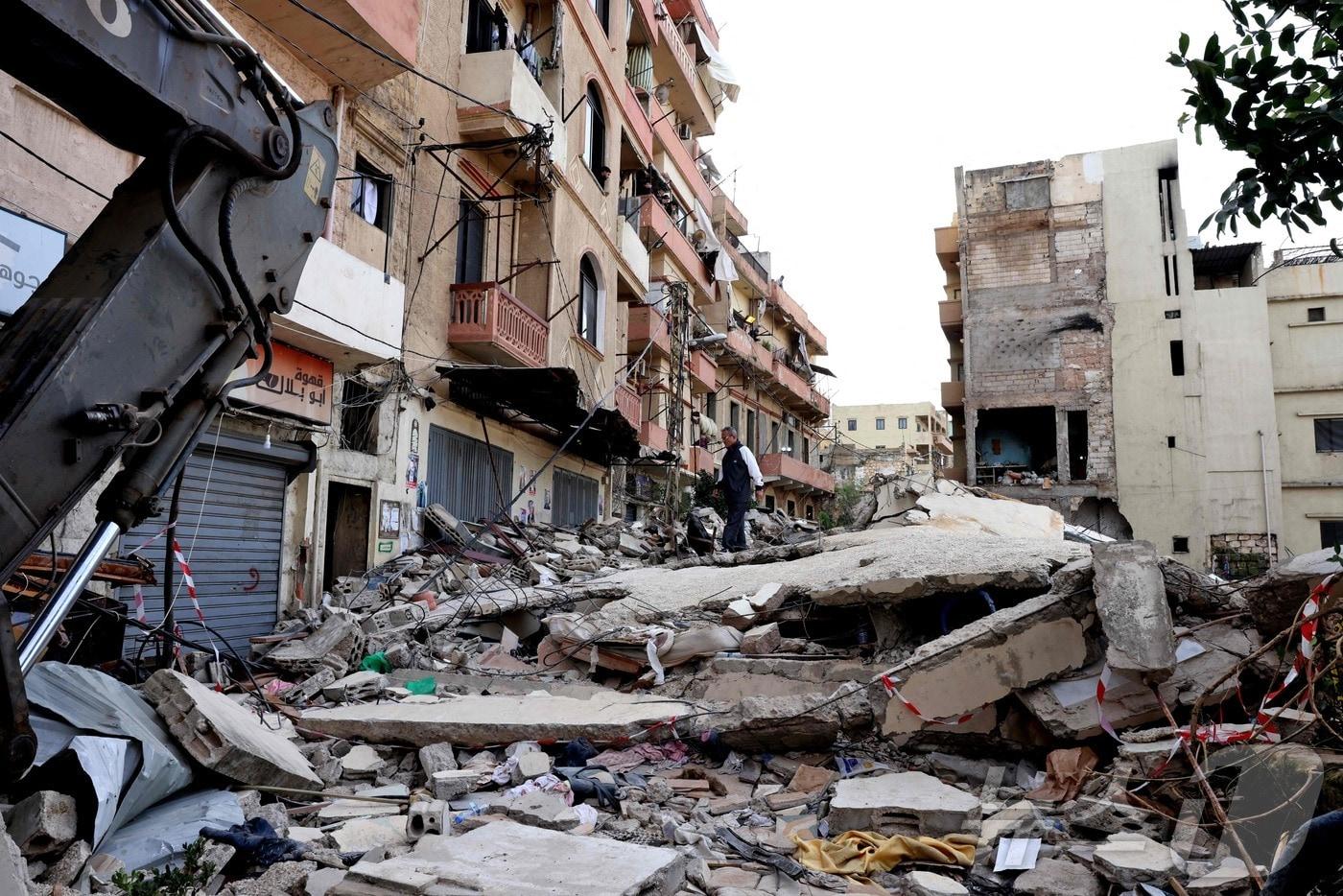 본문 이미지 - 9일(현지시간) 레바논 북부 도시 트리폴리의 바브 알 타바네 지역에서 붕괴된 오래된 주택 잔해 근처에 사람들이 서 있다. 2026.02.09. ⓒ AFP=뉴스1 ⓒ News1 이정환 기자