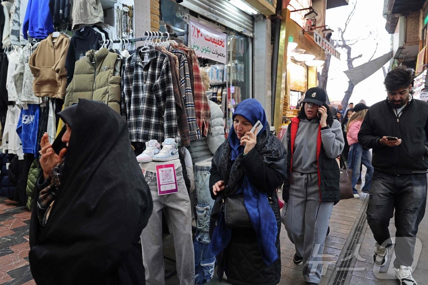 본문 이미지 - 2026년 1월 28일, 이란 테헤란 타지리시 바자르에서 사람들이 휴대전화를 사용하며 거리를 걷고 있다. ⓒ AFP=뉴스1