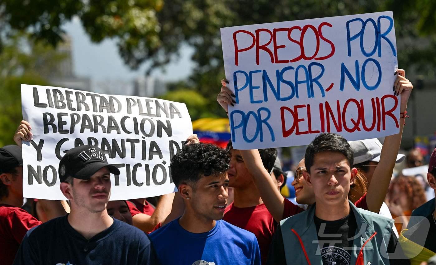 본문 이미지 - 12일(현지시간) 베네수엘라 수도 카라카스에서 열린 정치범 석방을 요구하는 시위에서 한 여성이 "범죄를 저질러서가 아니라 생각을 해서 감옥에 갇혔다＂라고 적힌 피켓을 들고 있다. '청년의 날'을 맞아 열린 이날 시위는 지난달 3일 미국이 니콜라스 마두로 대통령을 축출한 이후 열린 첫 반(反)정부 시위다. 2026.02.12 ⓒ AFP=뉴스1