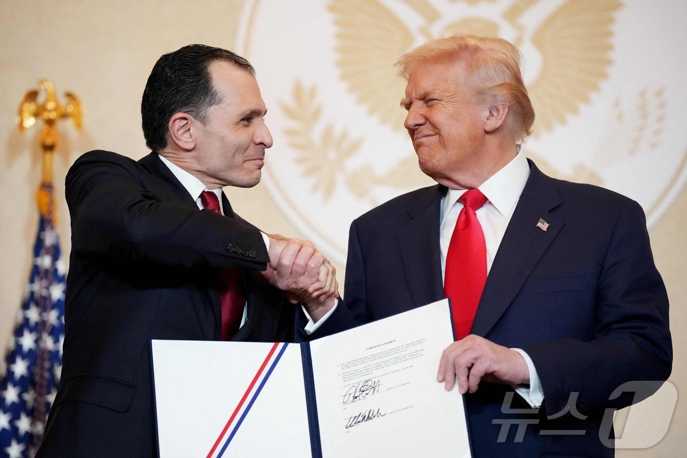 본문 이미지 - 2025년 10월 28일 일본 도쿄 주일 미국대사관저에서 열린 기업인 간담회에서 엔트라원(Entra1) 최고경영자 와디 하부시와 도널드 트럼프 미국 대통령이 양해각서(MOU) 서명 후 악수를 나누고 있다.2025.10.28.ⓒ AFP=뉴스1