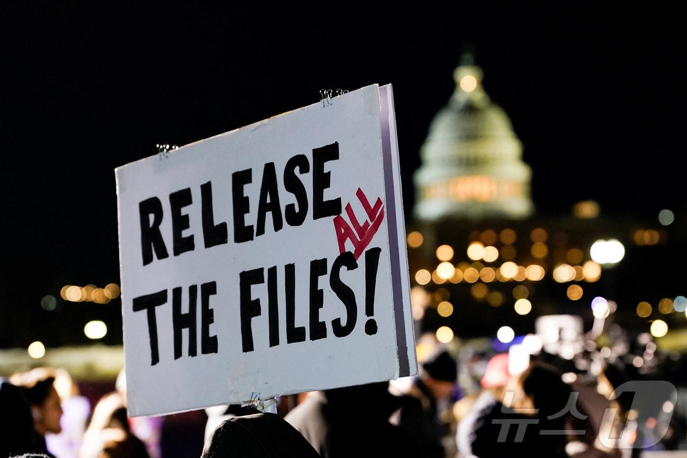 본문 이미지 - 도널드 트럼프 미국 대통령이 2기 임기 첫 국정연설을 진행한 24일(현지시간) 워싱턴DC에서 반대 차원의 '국민 국정연설'에서 한 사람이 '모든 파일을 해제하라'라고 쓰인 팻말을 들고 있다. 2026.2.24 ⓒ 로이터=뉴스1