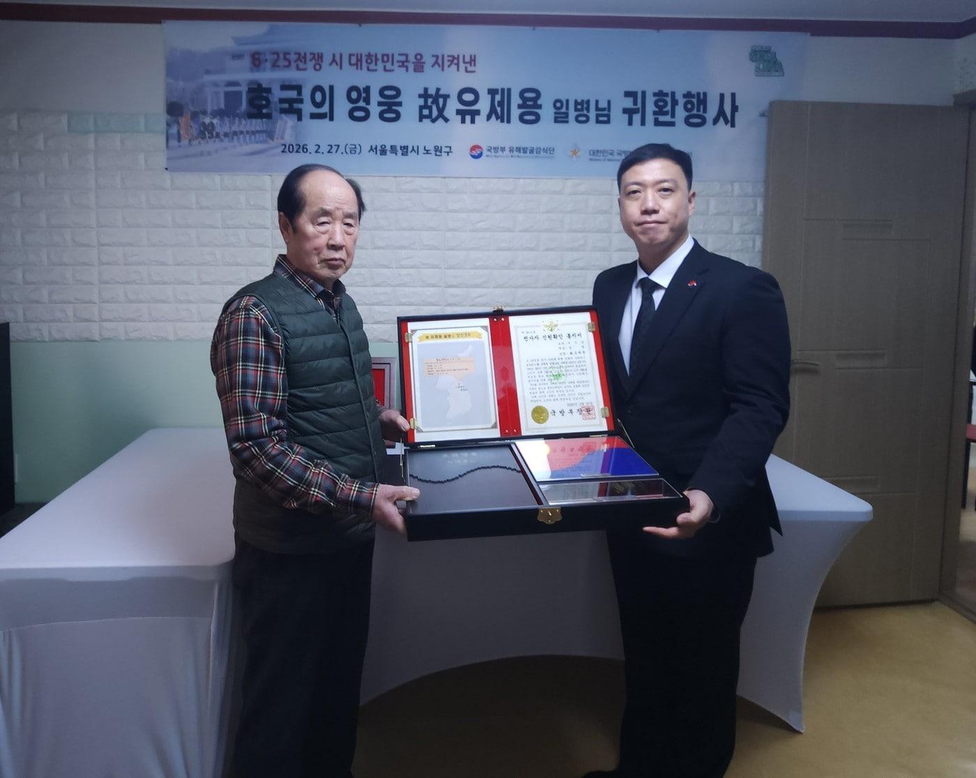본문 이미지 - 27일 서울특별시 노원구에 위치한 고 유제용 일병의 남동생 유제만 씨 자택에서 열린 호국의 영웅 귀환행사에서 김성환 국유단장 직무대리(오른쪽)와 유제만 씨(왼쪽)가 전사자 신원확인 통지서 등이 담긴 호국의 얼 함을 들고 기념사진을 촬영하고 있다.(국유단 제공)