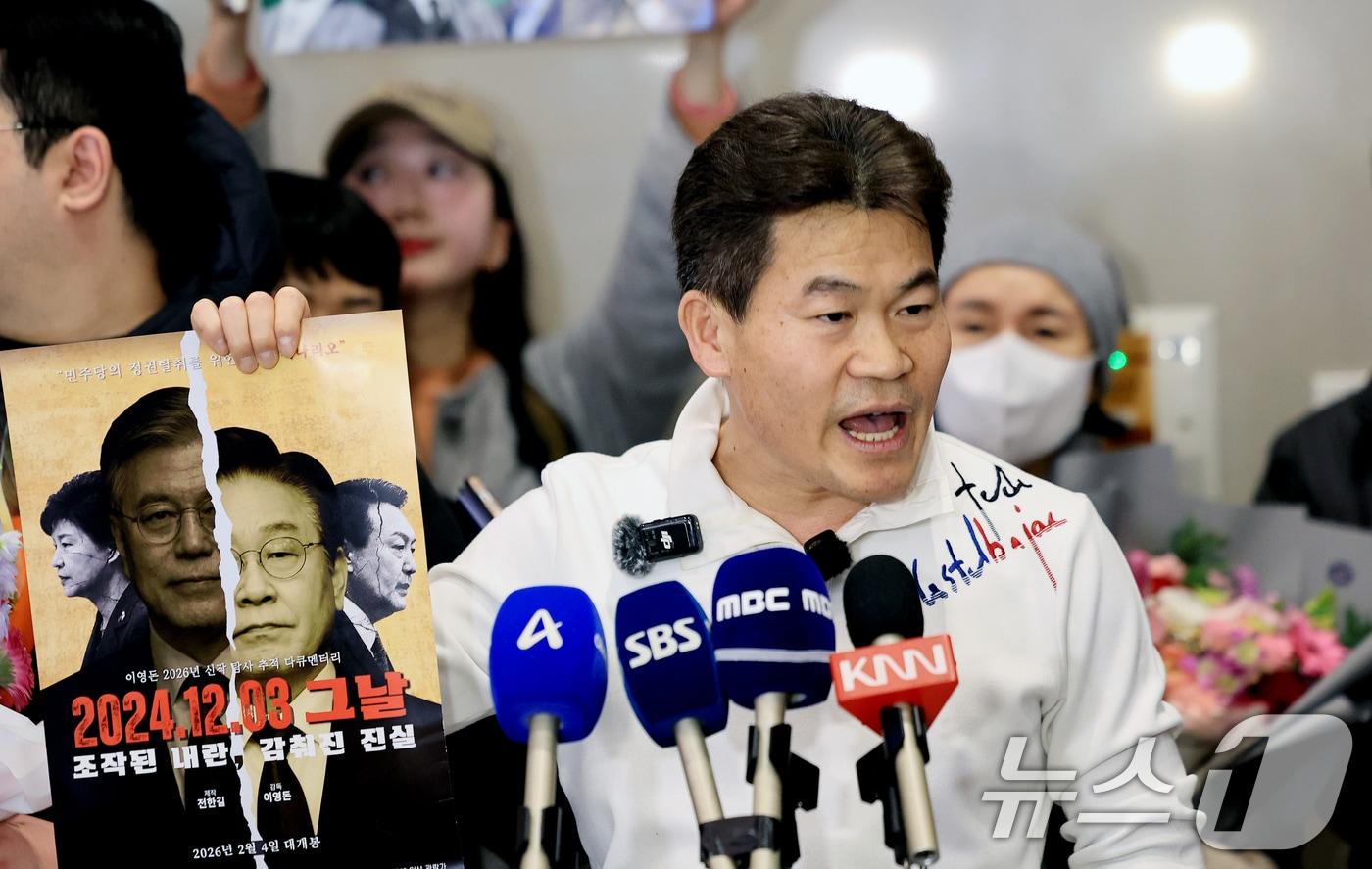 본문 이미지 - 전한길 전 한국사 강사가 3일 인천국제공항 제2여객터미널로 귀국해 기자회견에서 자신이 제작한 영화 포스터를 들어보이고 있다. 2026.2.3/뉴스1 ⓒ News1 이호윤 기자