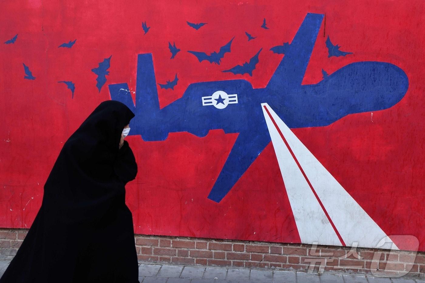 본문 이미지 - 한 여성이 2026년 2월 1일 테헤란 옛 미국 대사관 외벽에 그려진 미군 드론 벽화를 지나가고 있다. 같은 날 이란 최고지도자 아야톨라 알리 하메네이는 미국이 걸프 지역에 대규모 군사력을 배치한 뒤 공격에 나설 경우 전쟁이 벌어질 것이라고 경고했다.2026.02.01. ⓒ AFP=뉴스1