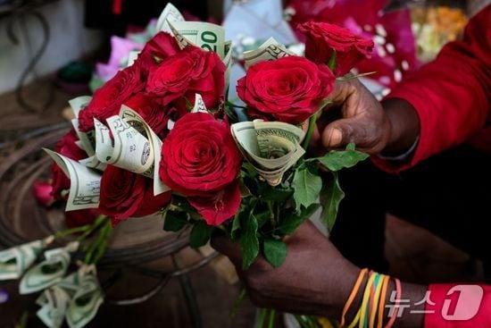 본문 이미지 - 짐바브웨 하라레의 꽃집에서 한 남성이 붉은 장미꽃과 20달러 지폐를 엮어 밸런타인 데이를 위한 '돈 꽃다발'을 준비했다. 2024.2.13 ⓒ AFP=뉴스1 ⓒ News1
