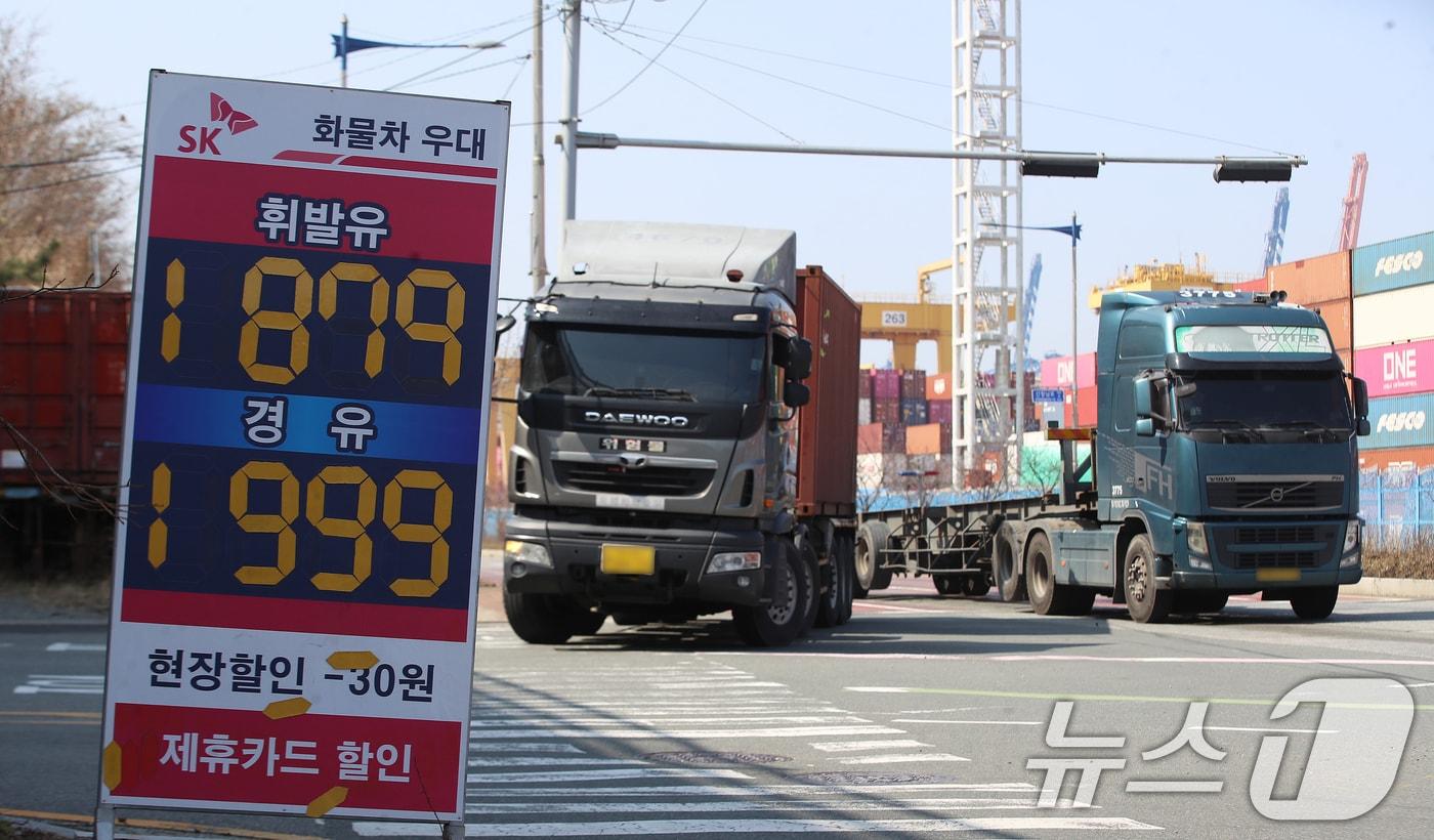 본문 이미지 - 중동 사태로 국제 유가가 급등하면서 유류비 부담이 커진 화물차 기사들이 어려움을 호소하고 있는 가운데 10일 경유 가격이 1999원으로 적혀 있는 부산 강서구 부산신항 인근 한 주유소 유가 안내판 뒤로 화물차들이 지나가고 있다. 2026.3.10 ⓒ 뉴스1 윤일지 기자