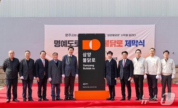 본문 이미지 - 강원 원주시가 지난 11일 우산동 삼양식품 원주공장 인근에서 원주시 제1호 명예도로명인 '삼양불닭로'의 제막식을 연 가운데, 원강수 원주시장과 김정수 삼양식품 부회장, 김동찬 삼양식품 대표 등 관계자 30여 명이 기념사진을 촬영하고 있다. (원주시 제공. 재판매 및 DB금지) 2026.3.12./뉴스1