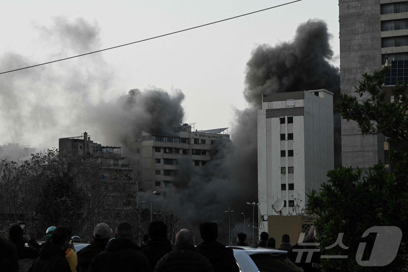 본문 이미지 - 이스라엘 미사일 공습 이후 12일(현지시간) 레바논 베이루트 중심가 바슈라(Bashoura) 지역 상공으로 연기가 치솟는 모습을 시민들이 바라보고 있다. 2026.03.12ⓒ AFP=뉴스1