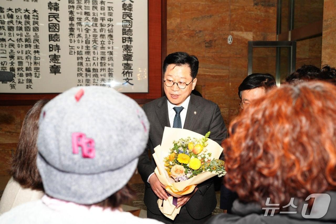 본문 이미지 -  '가습기살균제 피해 구제를 위한 특별법 전부개정안'의 본회의 통과 후 이를 대표 발의한 안호영 의원이 피해자들로부터 꽃다발을 받고 있다.(의회제공, 재판매 및 DB금지)2026.3.13/뉴스1