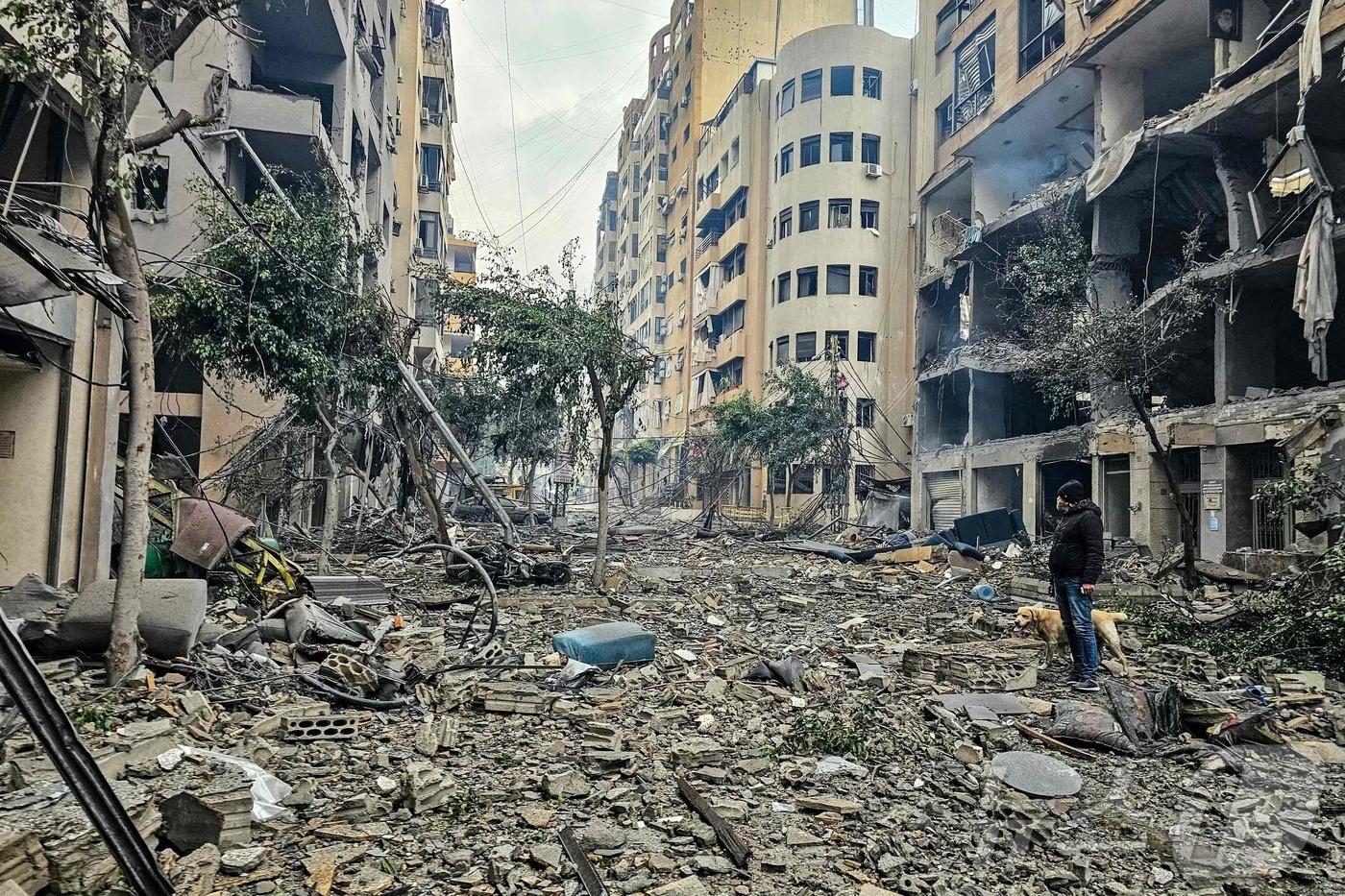 본문 이미지 - 2026년 3월 15일 레바논 베이루트 남부 교외 하레트 흐레이크에서 이스라엘 공습으로 파괴된 건물 잔해 위를 한 남성과 그의 반려견이 지나가고 있다.2026.03.15. ⓒ AFP=뉴스1