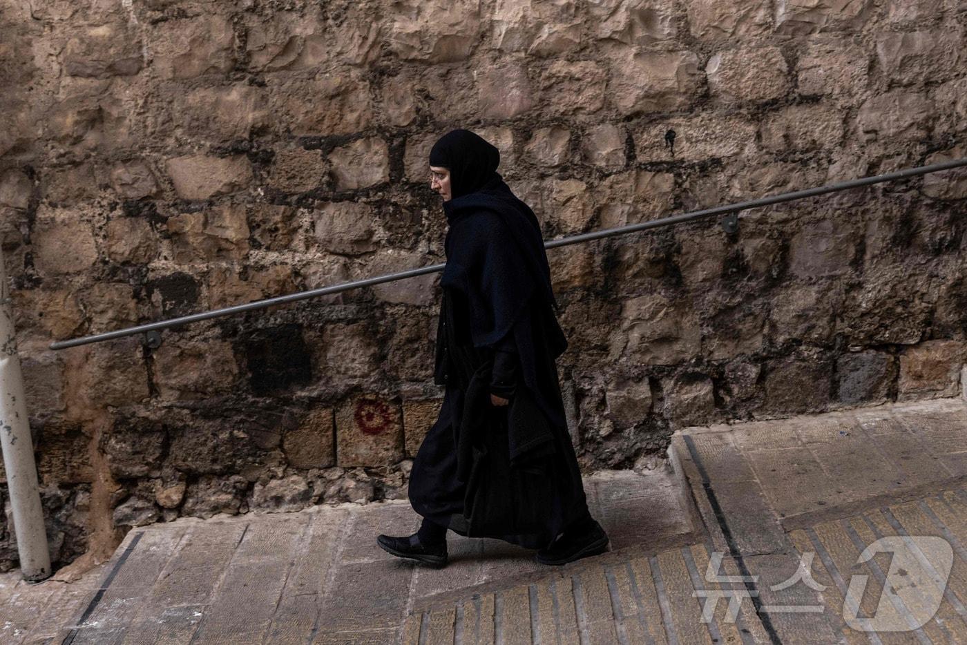 본문 이미지 - 16일(현지시간) 예루살렘 구시가지에 있는 그리스 정교회 총대주교청 담벼락을 따라 그리스 정교회 수녀가 걷고 있다. 이스라엘 경찰은 같은 날 예루살렘 구시가지의 성지, 특히 알 아크사 모스크와 성묘 교회 인근 지역에서 미사일과 요격기 파편을 발견했다고 밝혔다. 2026.03.16. ⓒ AFP=뉴스1