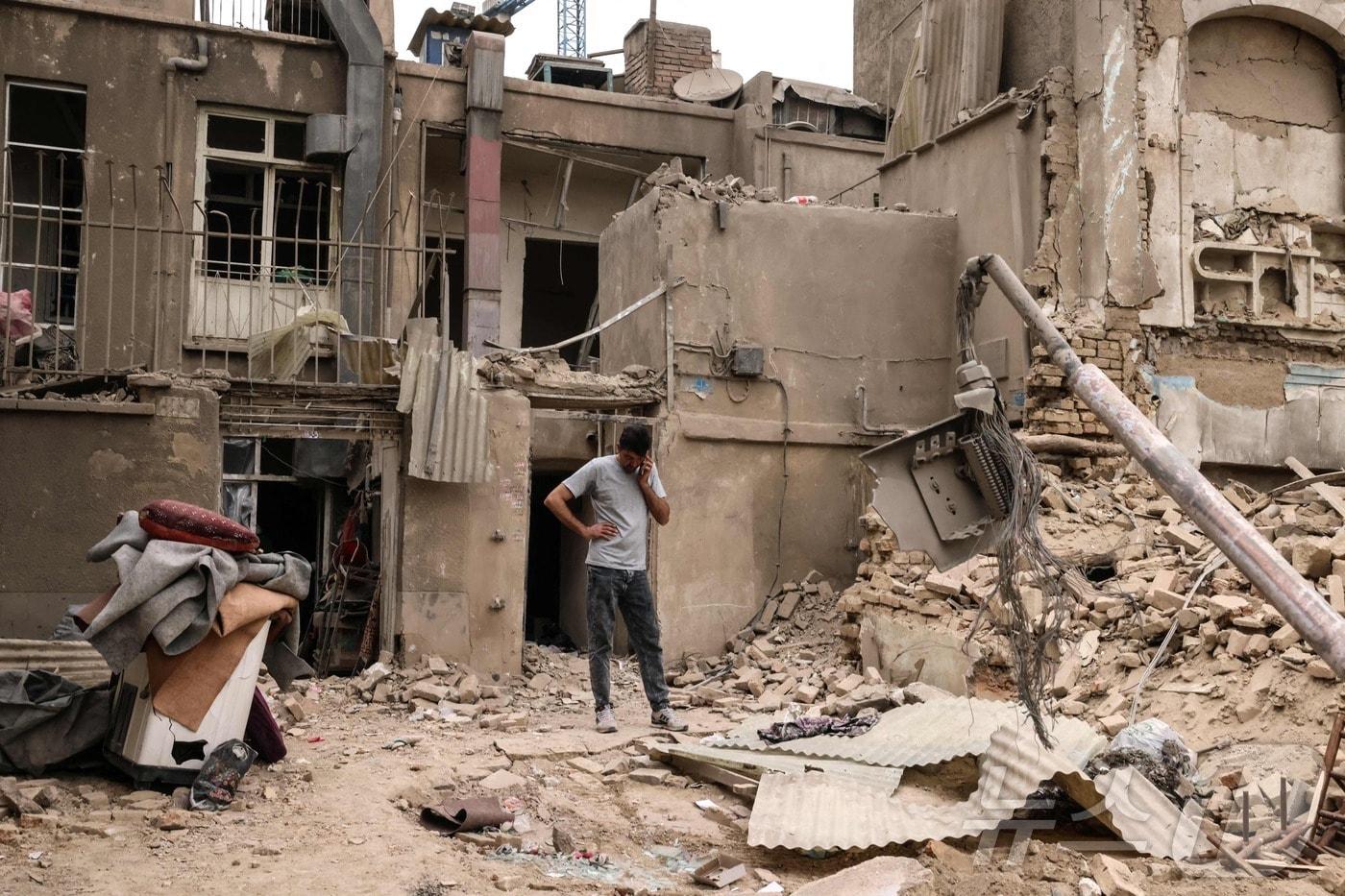 본문 이미지 - 15일(현지시간) 이란 수도 테헤란에 대한 군사 공습 이후, 한 남성이 파손된 주택들 밖에서 휴대전화로 통화하고 있다. 2026.03.15. ⓒ AFP=뉴스1