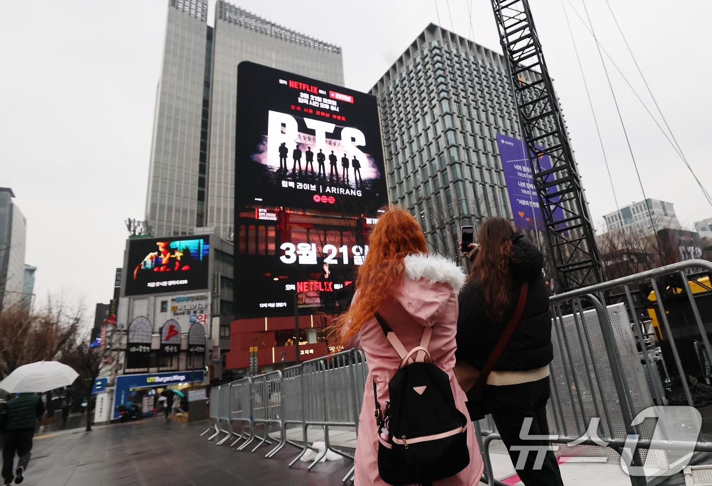 본문 이미지 - 방탄소년단(BTS) 완전체 컴백 공연을 사흘 앞둔 18일 서울 광화문광장에서 외국인 팬들이 컴백 공연을 알리는 전광판 광고를 스마트폰으로 촬영하고 있다. 정부는 이날 방탄소년단(BTS) 광화문 공연을 앞두고 19일 0시부터 21일 밤 12시까지 종로구와 중구 등 도심 일대 테러경보를 기존 '관심'에서 '주의'로 상향 발령한다고 밝혔다. 2026.3.18 ⓒ 뉴스1 오대일 기자