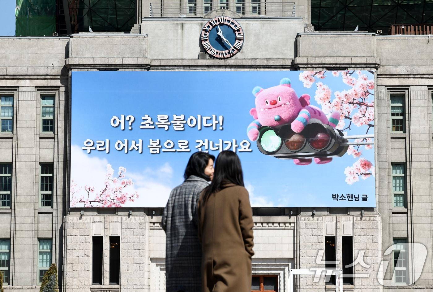 본문 이미지 - 서울 중구 서울도서관 외벽에 ‘어? 초록불이다! 우리, 어서 봄으로 건너가요’라는 문구가 적힌 서울꿈새김판이 걸려 있다. 2026.3.19 ⓒ 뉴스1 최지환 기자