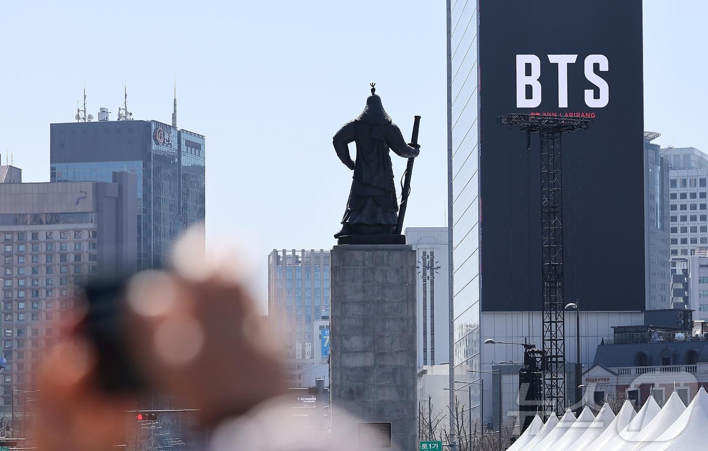 본문 이미지 - 방탄소년단(BTS)의 서울 광화문광장 컴백 공연이 이틀 앞으로 다가온 19일 서울 종로구 광화문광장에서 시민들이 한 건물 외벽에 부착된 BTS 컴백 공연 광고물을 스마트폰으로 촬영하고 있다. 2026.3.19 ⓒ 뉴스1 김성진 기자