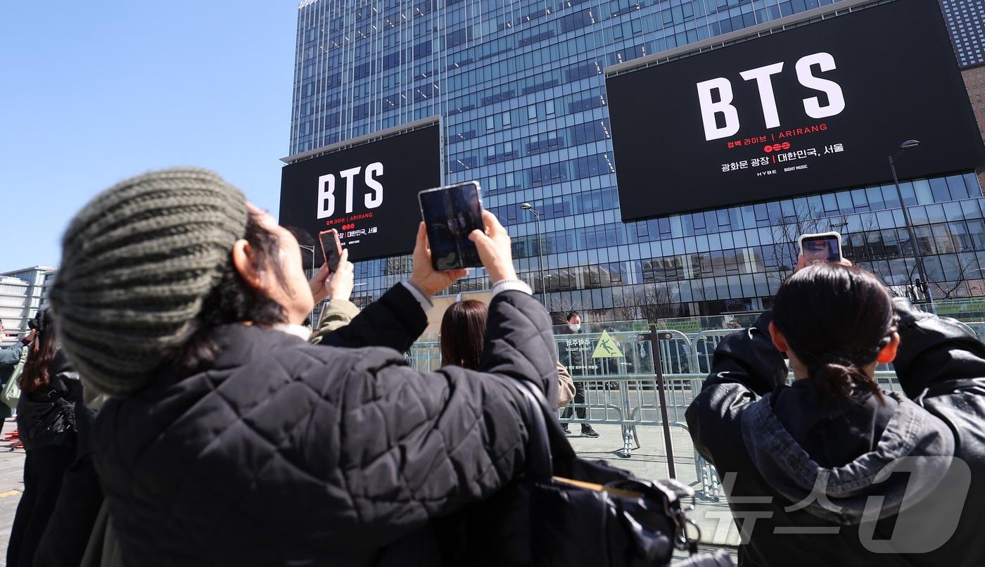 본문 이미지 - 방탄소년단(BTS)의 서울 광화문광장 컴백 공연이 이틀 앞으로 다가온 19일 서울 종로구 광화문광장에서 외국인 팬들이 컴백 공연을 알리는 전광판 광고를 스마트폰으로 촬영하고 있다. 2026.3.19 ⓒ 뉴스1 김성진 기자